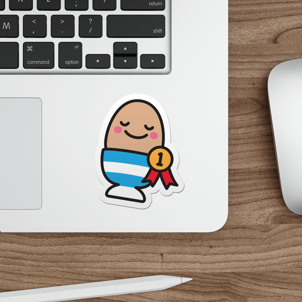 Laptop with a die-cute vinyl sticker of a good egg in a cup on a wooden desk.