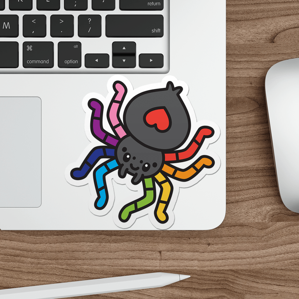 Colorful spider sticker on a laptop keyboard with a wooden desk.