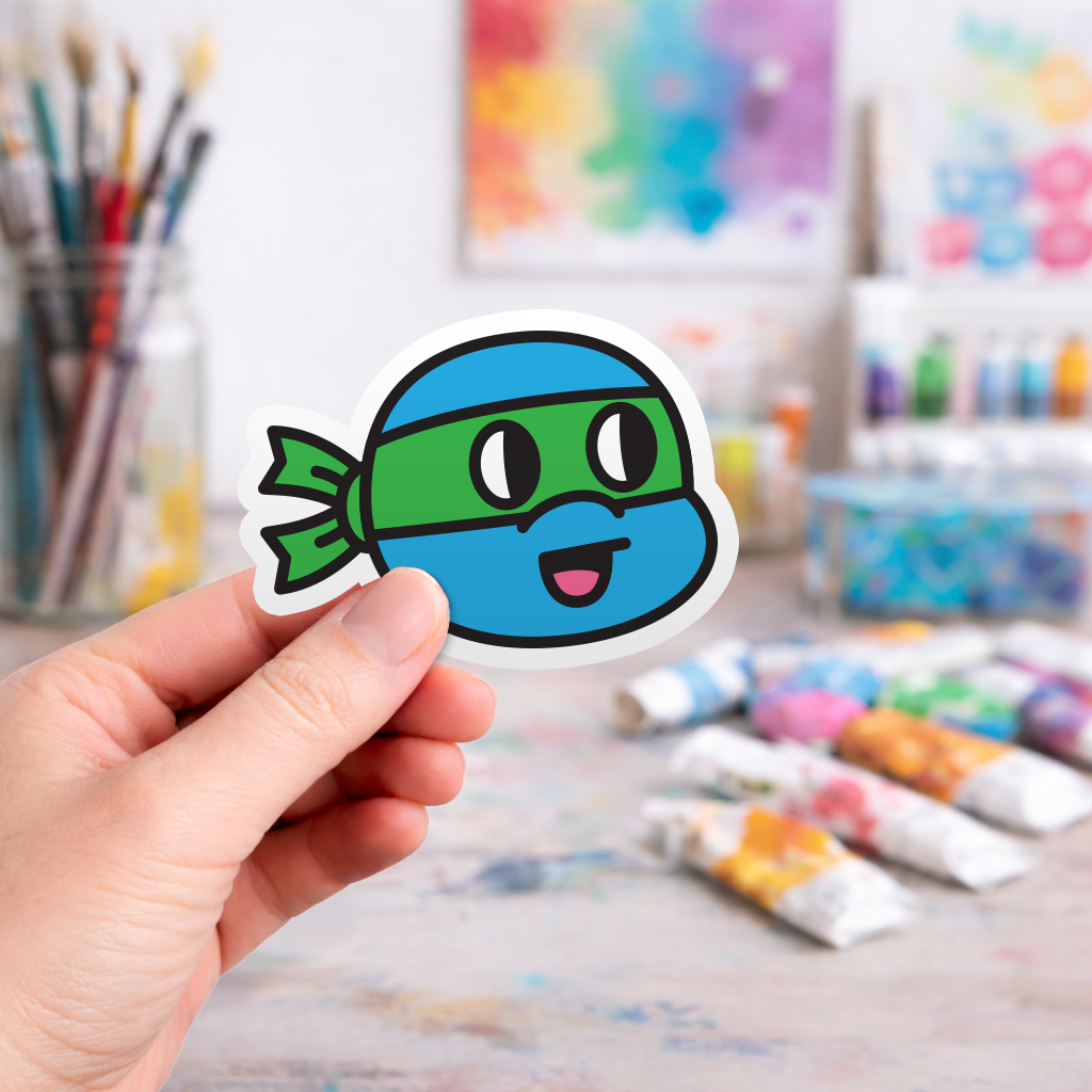 Hand holding a colorful laptop sticker of a cartoon ninja turtle character