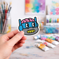 Hand holding a colorful laptop sticker of a cartoon ninja turtle character