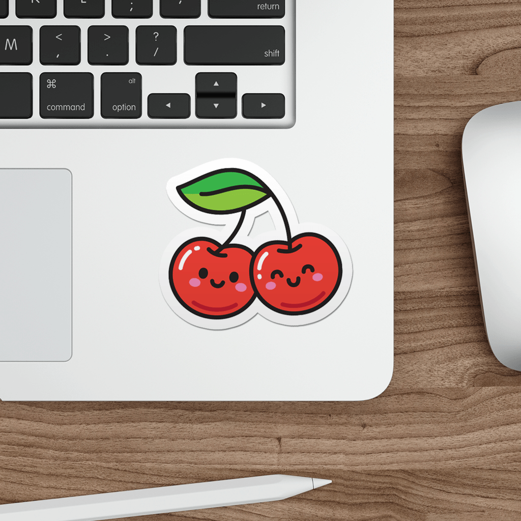 Laptop with a die-cut, vinyl sticker of a kawaii cherries on a wooden desk.