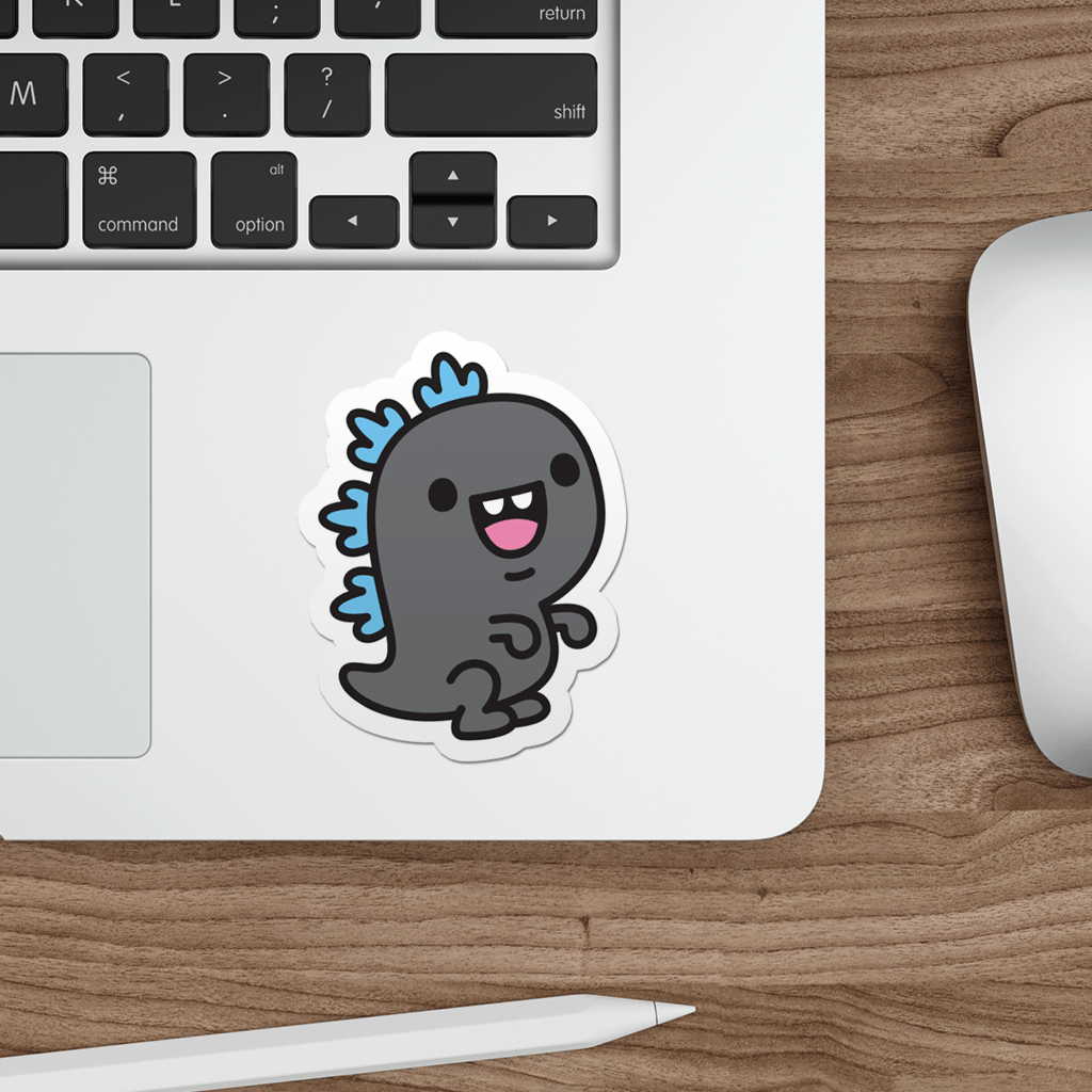 Laptop with a sticker of a kawaii godzilla dinosaur on a wooden desk.