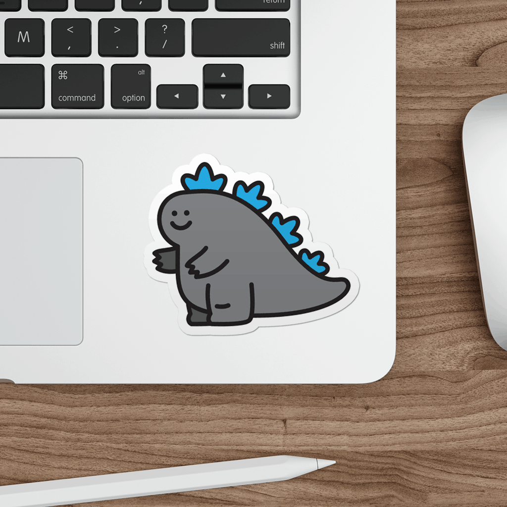 Laptop with a cute cartoon godzilla vinyl sticker on a wooden desk